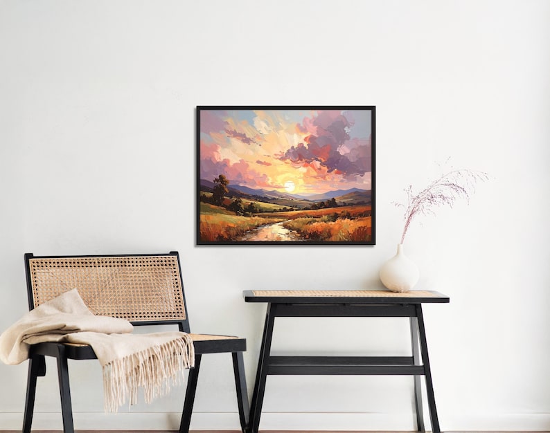 May include: A framed landscape painting depicts a sunset over a valley with a river. The sky is filled with pink, orange, and purple clouds. The foreground features golden fields and green hills.