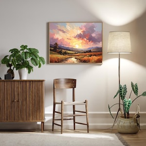 May include: A framed landscape painting depicts a sunset over a field and river. A wooden cabinet, chair, and floor lamp with a beige shade are in the room. A potted plant sits near the lamp, and another plant is on the cabinet.