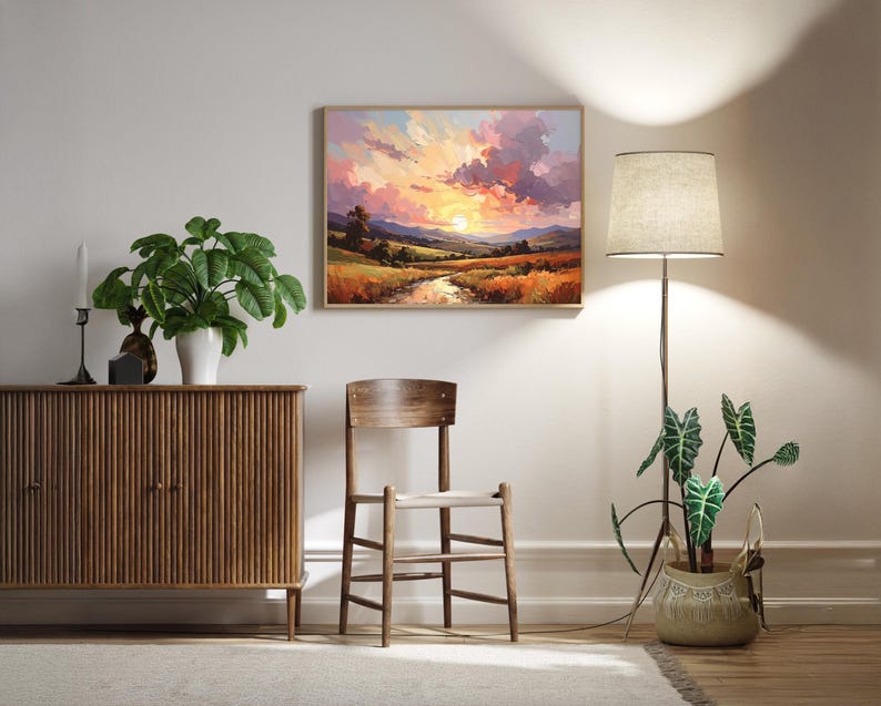 May include: A framed landscape painting depicts a sunset over a field and river. A wooden cabinet, chair, and floor lamp with a beige shade are in the room. A potted plant sits near the lamp, and another plant is on the cabinet.