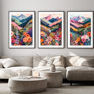 Può includere: Tre stampe artistiche incorniciate raffiguranti paesaggi montani colorati. Ogni stampa mostra una scena di montagna con fiori colorati in primo piano. L'opera d'arte è incorniciata in nero e appesa sopra un divano dai toni neutri.