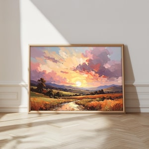 May include: A framed landscape painting depicts a sunset over a valley. The artwork features a vibrant sky with shades of orange, pink, and purple. A river flows through the foreground, with fields and trees in the mid-ground. The frame is a light brown color.