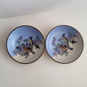 May include: Two small blue and white ceramic bowls with a floral design and birds. The bowls have a gold rim.