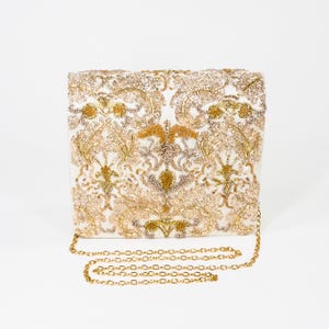 May include: A rectangular clutch bag featuring an intricate pattern of gold and champagne-colored beads and sequins on a white base. The bag includes a thin, detachable gold-tone metal chain strap with a classic link design for carrying.