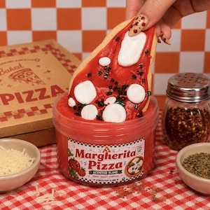 May include: A clear plastic jar of red Margherita Pizza scented slime with a label featuring the text Margherita Pizza, Fresh, Gooey, Stretchy, and Stress Pop Slime. A slice of pizza-shaped slime with white and green toppings is being lifted.