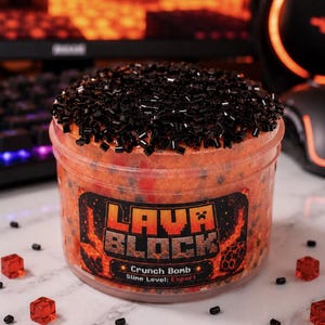 Puede incluir: Un frasco de plástico transparente lleno de slime naranja texturizado cubierto con cuentas cilíndricas negras. La etiqueta muestra el texto LAVA BLOCK, Crunch Bomb y Slime Level: Expert. Pequeños cubos rojos translúcidos y cuentas negras están esparcidos.