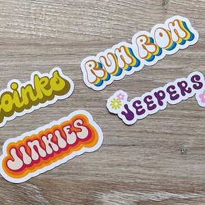 May include: Four colorful retro-style stickers with different phrases: "Zoinks", "Jinkies", "Ruh Roh", and "Jeepers". Each sticker has a white background and features a different color scheme.