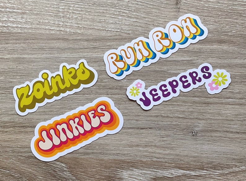 May include: Four colorful retro-style stickers with different phrases: "Zoinks", "Jinkies", "Ruh Roh", and "Jeepers". Each sticker has a white background and features a different color scheme.
