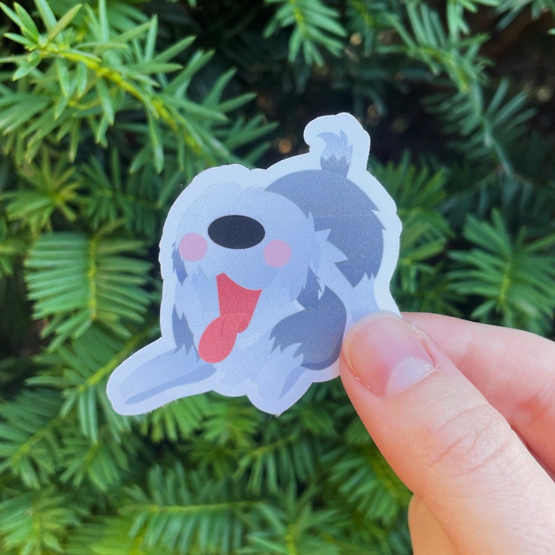 Pu&ograve; includere: Un adesivo di un cane di cartone animato con pelliccia grigia, naso rosa e lingua rossa che sporge. Il cane &egrave; seduto sulle zampe posteriori con le zampe anteriori in aria.