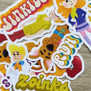 May include: A collection of colorful cartoon character stickers featuring Scooby Doo, Shaggy, and other characters from the Scooby Doo franchise. The stickers feature the words "Jinkies", "Zoinks", and "Ruh Roh".