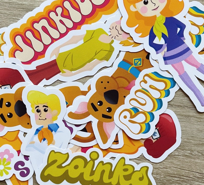 May include: A collection of colorful cartoon character stickers featuring Scooby Doo, Shaggy, and other characters from the Scooby Doo franchise. The stickers feature the words "Jinkies", "Zoinks", and "Ruh Roh".