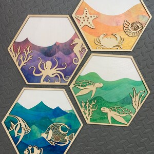Pode incluir: Quatro pe&ccedil;as de decora&ccedil;&atilde;o de parede hexagonal de madeira com fundos de aquarela e criaturas marinhas recortadas. A pe&ccedil;a superior apresenta uma estrela do mar, uma concha e um caranguejo. A pe&ccedil;a seguinte apresenta um polvo, coral e um cavalo-marinho. A terceira pe&ccedil;a apresenta duas tartarugas marinhas e coral. A pe&ccedil;a inferior apresenta um peixe-palha&ccedil;o, um peixe-anjo e um peixe-borboleta.