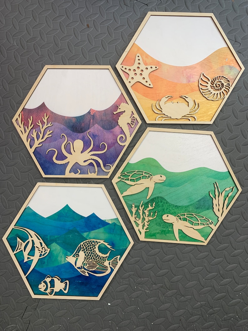 Pode incluir: Quatro pe&ccedil;as de decora&ccedil;&atilde;o de parede hexagonal de madeira com fundos de aquarela e criaturas marinhas recortadas. A pe&ccedil;a superior apresenta uma estrela do mar, uma concha e um caranguejo. A pe&ccedil;a seguinte apresenta um polvo, coral e um cavalo-marinho. A terceira pe&ccedil;a apresenta duas tartarugas marinhas e coral. A pe&ccedil;a inferior apresenta um peixe-palha&ccedil;o, um peixe-anjo e um peixe-borboleta.
