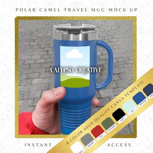 May include: A blue travel mug with a stainless steel lid and a handle. The mug has a white cloud and green hills design on the front. The text "CALYPSO CREATIVE" is printed on the mug. The mug is being held by a hand.