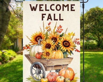 Op de afbeelding: Een herfst-tuin vlag met een witte achtergrond en bruine tekst. De tekst zegt "Welkom Herfst". De vlag heeft een aquarel illustratie van een houten kar vol met zonnebloemen en pompoenen.
