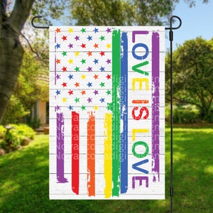 Puede incluir: Una bandera de jardín blanca con un diseño de bandera estadounidense de colores arcoíris y el texto "Love is Love" en una fuente desgastada.