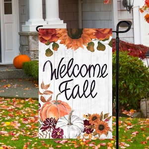 May include: Welcome Fall garden flag with a white wood background, featuring pumpkins, sunflowers, and burgundy flowers.