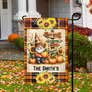 May include: A fall-themed garden flag with a plaid background. It features a gnome holding a pumpkin, sunflowers, and a sign that reads "Happy Harvest". The flag also includes the text "The Smith's".