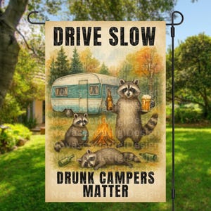Könnte beinhalten: Eine Gartenflagge mit dem Text "DRIVE SLOW DRUNK CAMPERS MATTER" und einer Aquarellillustration von campierenden Waschbären. Ein Waschbär hält ein Bier, ein anderer eine Flasche, und ein dritter liegt. Ein Wohnwagen und ein Lagerfeuer sind ebenfalls abgebildet.