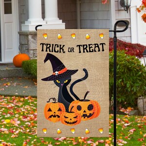 May include: A burlap garden flag featuring a black cat wearing a witch's hat and holding a pumpkin. The flag reads "Trick or Treat" in a vintage font. Candy corn accents adorn the border.