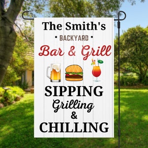 May include: A white wooden sign with red text that reads "The Smith's Backyard Bar & Grill Sipping Grilling & Chilling". The sign has a beer mug, hamburger, and a cocktail glass with a red drink and a straw.