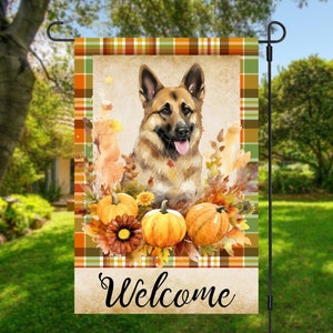 May include: A welcome garden flag with a German Shepherd dog surrounded by fall leaves and pumpkins. The flag has a plaid border and the word "Welcome" at the bottom.