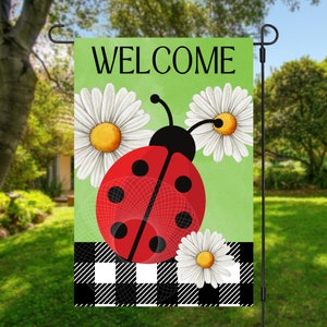 May include: A green welcome garden flag with a red ladybug, black dots, and white daisies. The flag has a black and white checkered pattern at the bottom.