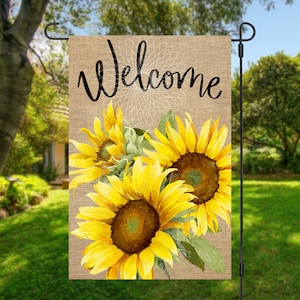 May include: A burlap garden flag with the word "Welcome" in black script and a watercolour illustration of three yellow sunflowers.