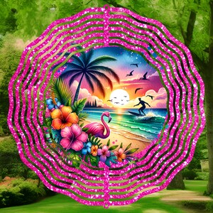 Op de afbeelding: Een roze glitter windmolen met een tropische zonsondergang scène met een roze flamingo, palmbomen en een surfer. De scène is omringd door roze, groene en gele bloemen.