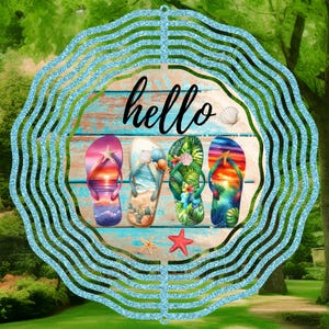 May include: A blue and white metal wind spinner with a wooden circle in the center. The circle has the word "hello" written on it and four colorful flip flops. The flip flops have different designs, including a sunset, a beach scene, and tropical leaves.