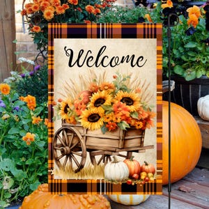 May include: A welcome garden flag with a plaid border features a vintage-style illustration of a wooden wagon overflowing with sunflowers, wheat, and pumpkins. The wagon is on a grassy field with a brown background.