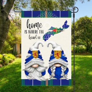 May include: A garden flag with a white background and a blue and green tartan border. The flag features two gnomes wearing blue and white hats with the Scottish flag on them. The flag also features a map of Nova Scotia with the Scottish flag on it. The text "home is where the heart is" is written in black on the flag.