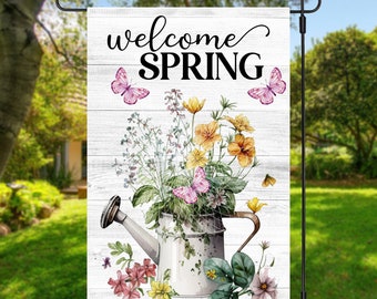 May include: A white wooden sign with the text "welcome spring" in black cursive lettering. A vintage watering can filled with colourful flowers and butterflies is in the centre of the sign.