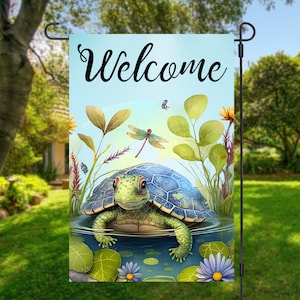 May include: A welcome garden flag with a blue and green turtle swimming in a pond with green lily pads and a dragonfly flying above. The flag has a blue background with the word "Welcome" in black cursive lettering.