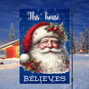 Puede incluir: Una bandera de jardín navideña azul con un borde blanco y una imagen de Santa Claus. La bandera dice "Esta casa cree".