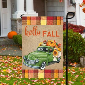 May include: A burlap garden flag with a green vintage truck carrying pumpkins, sunflowers, and fall leaves. The flag has a plaid border and says "hello FALL" in brown text.