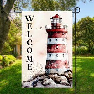 May include: A watercolor-style garden flag with a red and white lighthouse on a rocky shore. The text "WELCOME" is written vertically on the left side of the flag.
