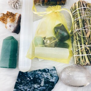 Puede incluir: Una colecci&oacute;n de cristales y piedras, que incluye una varita de selenita, una punta de aventurina verde, un cuarzo claro, una piedra de ojo de tigre en una botella de vidrio, una &aacute;gata verde musgosa y un palo de salvia.