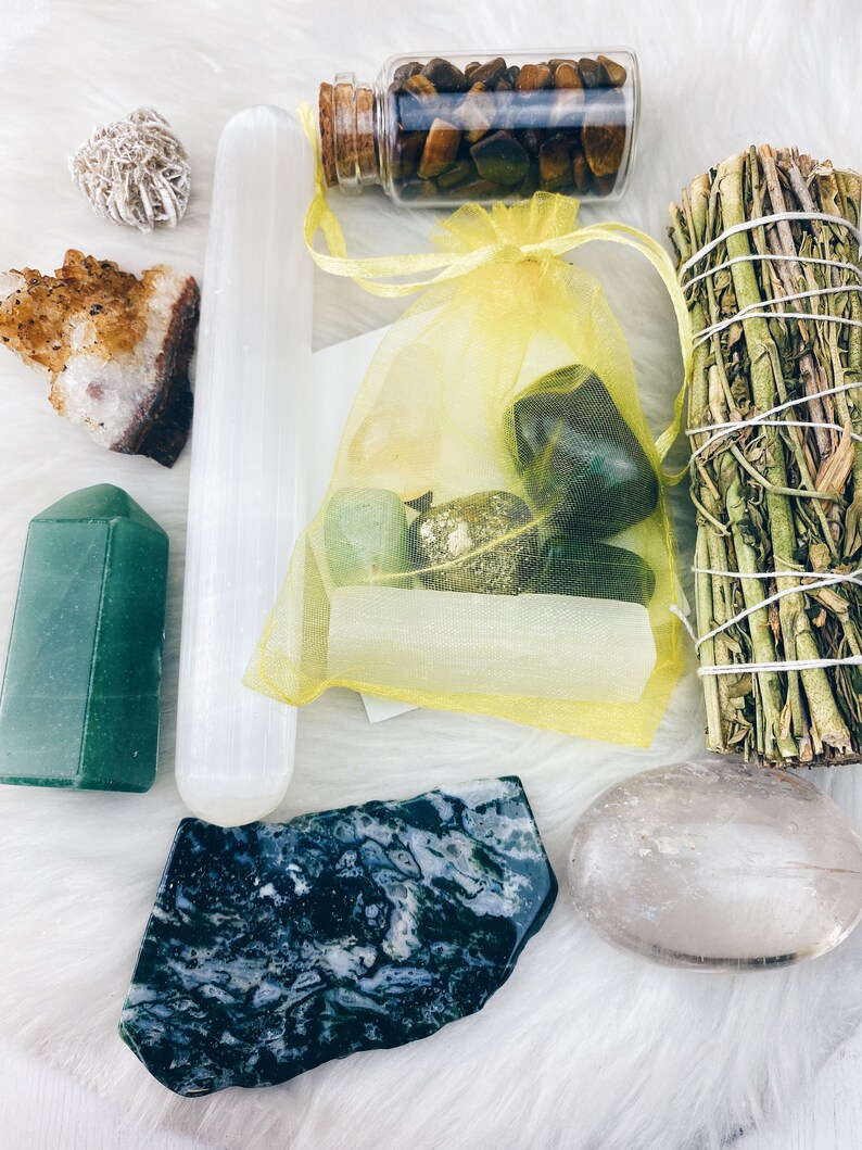 Puede incluir: Una colecci&oacute;n de cristales y piedras, que incluye una varita de selenita, una punta de aventurina verde, un cuarzo claro, una piedra de ojo de tigre en una botella de vidrio, una &aacute;gata verde musgosa y un palo de salvia.