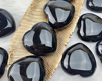 May include: A collection of black obsidian heart-shaped stones on a gold leaf patterned surface. The stones are polished and have a glossy finish.