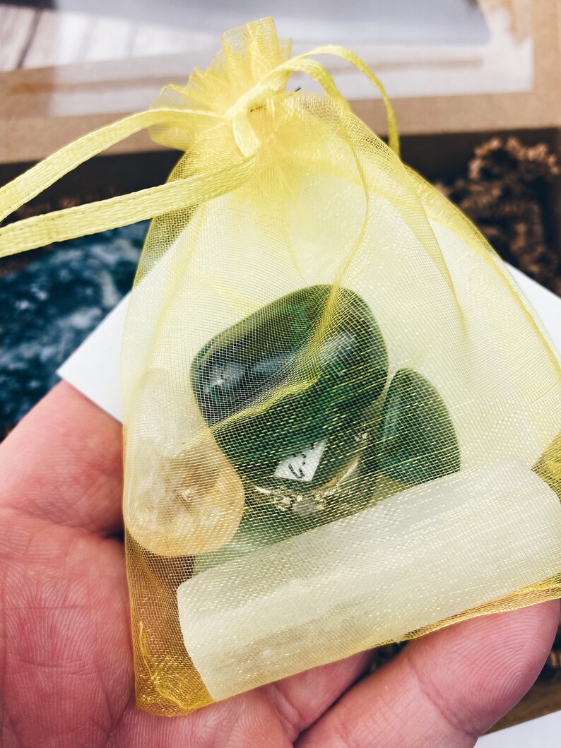 Puede incluir: Una bolsa de organza amarilla llena de cristales verdes, blancos y transparentes. Los cristales est&aacute;n pulidos y redondeados.