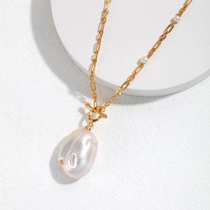 May include: A gold chain necklace with a large, irregular pearl pendant. The chain has small pearl accents.