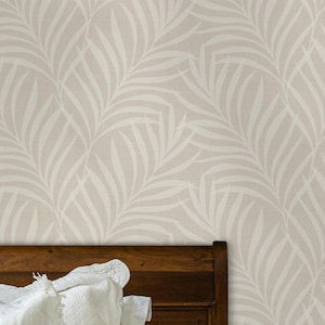 May include: Wallpaper featuring a repeating pattern of light beige palm leaves on a cream background. The design is displayed behind a dark wood headboard with white pillows and a white bedspread, showcasing the botanical print on the wall.