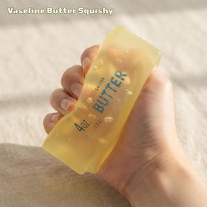 Puede incluir: Un juguete squishy amarillo translúcido con forma de barra de mantequilla. El texto en la superficie dice Salted Butter, 4 oz. y 113 g. El material es suave y flexible, mostrando pequeñas burbujas de aire dentro del cuerpo amarillo semitransparente.