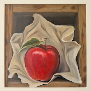 May include: An oil painting of a single bright red apple with a green leaf on its stem, resting on a piece of off-white fabric inside a wooden box frame. The artist's signature, Tina Kim, is visible in the bottom right corner of the canvas.