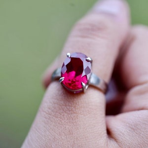 May include: A silver ring with a large, oval-shaped, deep red gemstone.