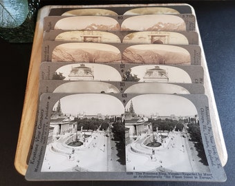 Puede incluir: Un conjunto de tarjetas estereoscópicas antiguas con fotografías en blanco y negro de varios lugares. Las tarjetas están en una caja de madera y tienen una etiqueta de Keystone View Company. El texto en las tarjetas dice "The Franzens-Ring, Vienna-Regarded by Many as Architecturally "the Finest Street in Europe."