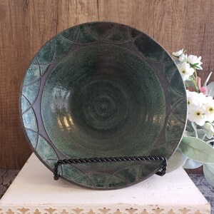 Puede incluir: Un cuenco de cerámica verde oscuro con un diseño decorativo alrededor del borde. El cuenco está sobre un soporte blanco con un borde decorativo.
