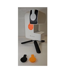 Może przedstawiać: Biała kamera 3D z czarną osłoną obiektywu i czarnym statywem. Kamera ma logo SeeStar i napis "3.0" z boku. Dwa małe okrągłe przedmioty, jeden czarny, a drugi pomarańczowy, znajdują się na pierwszym planie.