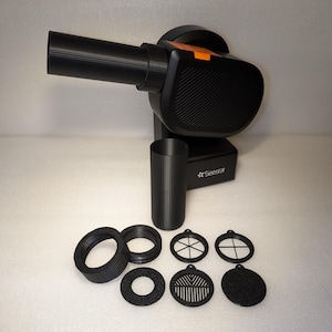 Może przedstawiać: Czarno-pomarańczowy elektryczny dmuchawa do liści z różnymi czarnymi plastikowymi końcówkami, w tym dyszą, okrągłym filtrem i filtrem z siatką. Dmuchawa jest oznaczona "SeeStar".