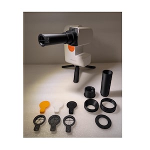 Könnte beinhalten: Ein weißer Projektor mit einem schwarzen Objektiv und einem Stativ. Der Projektor steht auf einer weißen Oberfläche mit verschiedenen schwarzen und weißen Plastik-Scheiben und einem schwarzen Rohr.